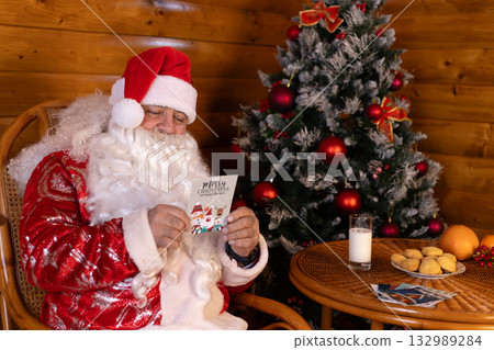 Santa Claus is sitting in a chair and reading a Christmas card 132989284