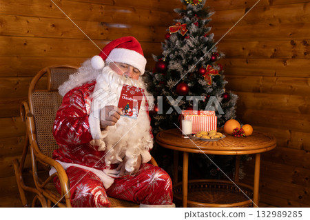 Santa holds a Christmas card in his hands while sitting on a chair 132989285