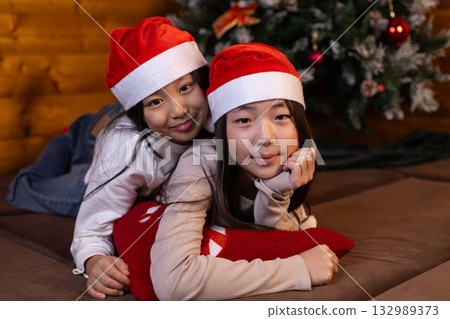 Two girls wearing Santa hats are smiling and posing together for a photo Two girls wearing Santa hats are smiling and posing together for a photo 132989373