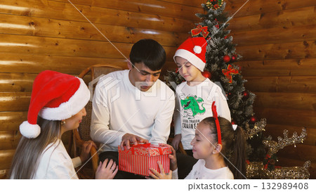 Family joyfully unwrapping a Christmas gift together Family joyfully unwrapping a Christmas gift together 132989408