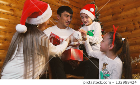 family wearing Santa hats is joyfully celebrating Christmas by exchanging gifts family wearing Santa hats is joyfully celebrating Christmas by exchanging gifts 132989424