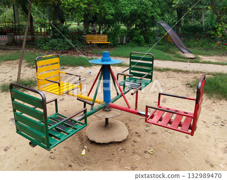 Colorful metal merry-go-round with four seats in park playground, green, yellow, and red, central rotating axis, fun outdoor equipment for children Colorful metal merry-go-round with four seats in park playground, green, yellow, and red, central rotating axis, fun outdoor equipment for children 132989470