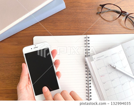 A woman's hand holding a schedule book and a smartphone on her desk A woman's hand holding a schedule book and a smartphone on her desk 132994035