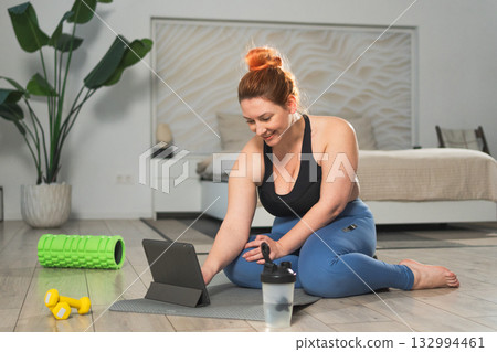 Yoga fitness workout training online. Woman practicing stretching with online app lessons at home. Plus size female doing sports exercise on yoga mat indoor. Girl have training workout for weight loss Yoga fitness workout training online. Woman practicing stretching with online app lessons at home. Plus size female doing sports exercise on yoga mat indoor. Girl have training workout for weight loss 132994461