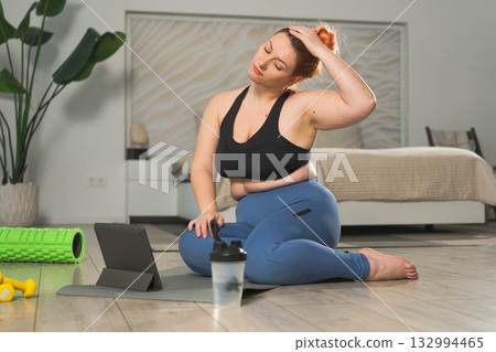 Yoga fitness workout training online. Woman practicing stretching with online app lessons at home. Plus size female doing sports exercise on yoga mat indoor. Girl have training workout for weight loss 132994465