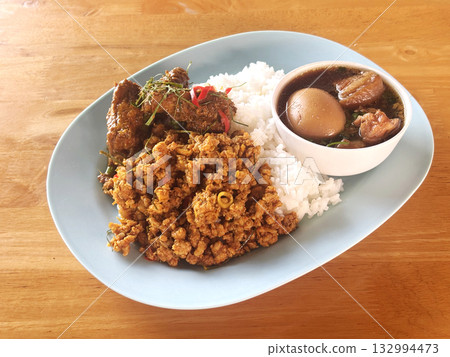 Thai-style meal featuring various traditionalThai-style meal featuring various traditional dishes served over rice on a single plate dishes served over rice 132994473