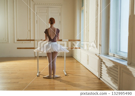 Young ballerina in tutu skirt stretching practicing ballet positions dancing near ballet barre in dance class. Young classical dancer woman in dance studio. Ballet class training Ballet school concept Young ballerina in tutu skirt stretching practicing ballet positions dancing near ballet barre in dance class. Young classical dancer woman in dance studio. Ballet class training Ballet school concept 132995490
