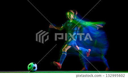 Female soccer player kicking ball in glowing teal and green motion blur 132995602