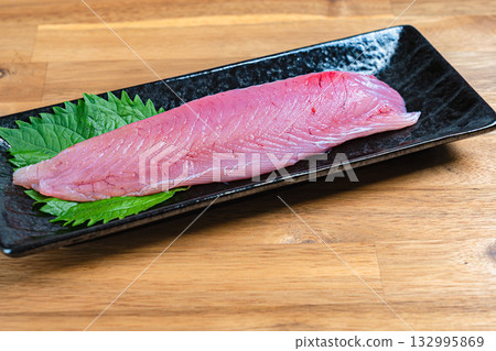 Strips of skipjack tuna, raw tuna and shiso leaves on a long black plate Strips of skipjack tuna, raw tuna and shiso leaves on a long black plate 132995869