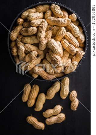 Peanuts in shell. Groundnuts in bowl on black table. Top view. Peanuts in shell. Groundnuts in bowl on black table. Top view. 132995895