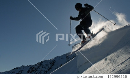 Professional skier jumping from snowy mountain ridge in bright sunlight Professional skier jumping from snowy mountain ridge in bright sunlight 132996216