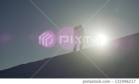 Determined mountaineer ascending snowy slope against sunlight Determined mountaineer ascending snowy slope against sunlight 132996217