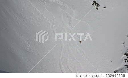 Skier leaving tracks on pristine snow field near rocky cliffs 132996236