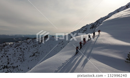 Adventurers climbing snowy mountain ridge in scenic winter landscape Adventurers climbing snowy mountain ridge in scenic winter landscape 132996240