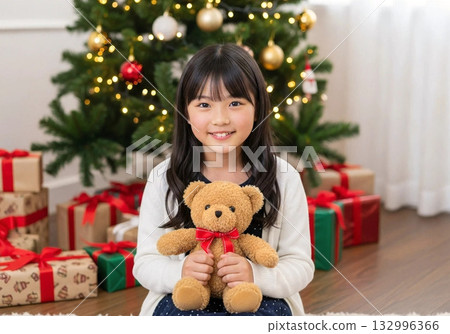 A little girl hugging a teddy bear as a gift with a Christmas tree in the background A little girl hugging a teddy bear as a gift with a Christmas tree in the background 132996366