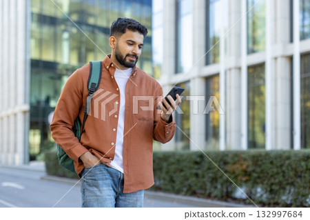 A stylish individual stands outdoors, browsing on a smartphone with modern architecture in the background, exuding an urban and youthful vibe. A stylish individual stands outdoors, browsing on a smartphone with modern architecture in the background, exuding an urban and youthful vibe. 132997684