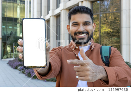 Indian man presenting a blank smartphone screen with a pointing gesture, ready for custom content while standing outdoors, representing modern technology and communication concepts Indian man presenting a blank smartphone screen with a pointing gesture, ready for custom content while standing outdoors, representing modern technology and communication concepts 132997686