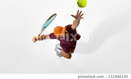 Focused tennis player in burgundy clothing jumping for serve on minimal white background Focused tennis player in burgundy clothing jumping for serve on minimal white background 132998149