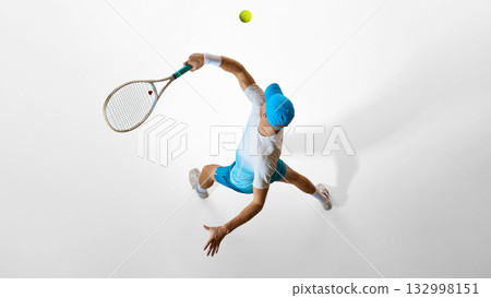 Tennis player in bright blue uniform preparing serve captured from above on white studio floor 132998151