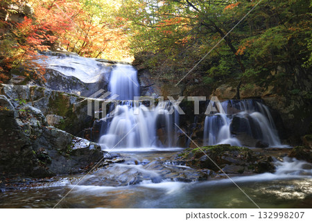 A waterfall in a valley  colored with autumn leaves. 132998207