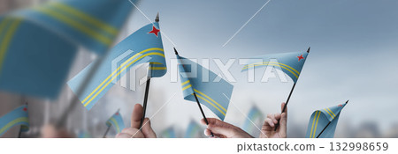 Aruba flags in their hands on a blurred urban background 132998659