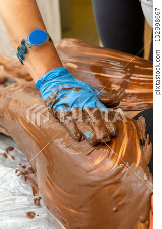 A therapist applies a rich chocolate body wrap treatment to a person 132998667