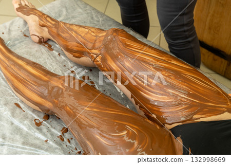 A therapist applies a rich chocolate body wrap treatment to a person A therapist applies a rich chocolate body wrap treatment to a person 132998669