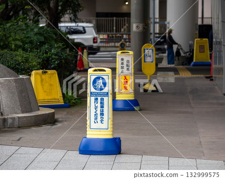 A sign stand placed on the grounds of a public facility reads, "Please dismount your bicycle before passing through." A sign stand placed on the grounds of a public facility reads, "Please dismount your bicycle before passing through." 132999575