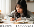 Woman in a gray sweater writing a letter in bright light by the window 132999583