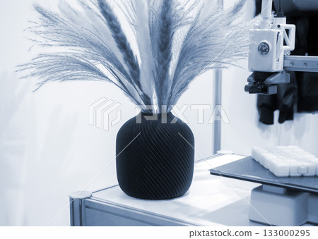 Beautiful dark vase with dried flowers printed on 3D printer on table. Model created by 3D printer from molten plastic. 3D printing technology. New modern additive progressive FDM printing technology 133000295