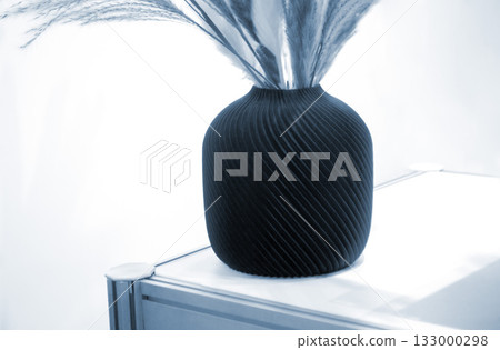 Beautiful dark vase with dried flowers printed on 3D printer on table. Model created by 3D printer from molten plastic. 3D printing technology. New modern additive progressive FDM printing technology Beautiful dark vase with dried flowers printed on 3D printer on table. Model created by 3D printer from molten plastic. 3D printing technology. New modern additive progressive FDM printing technology 133000298