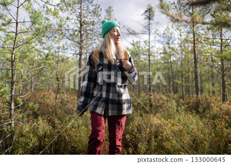 Spiritual woman hiker with backpack searching for trail in autumn boggy woodland, looking around 133000645