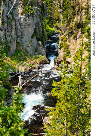 Vertical view of Kepler Cascades in Yellowstone National Park. The Firehole River rushes through a narrow rock canyon, surrounded by a dense green pine forest Vertical view of Kepler Cascades in Yellowstone National Park. The Firehole River rushes through a narrow rock canyon, surrounded by a dense green pine forest 133000757
