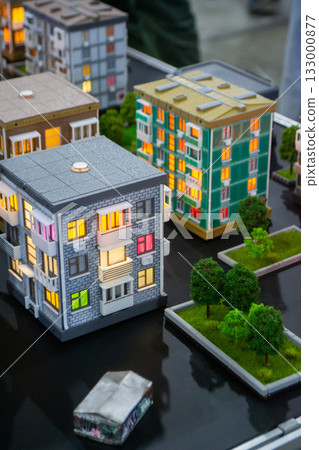 Prototype building printed on 3D printer from melted plastic. 3D-printed building prototype. A house created on 3D printer with gray walls, gray roof, and illuminated windows and balconies. 133000877