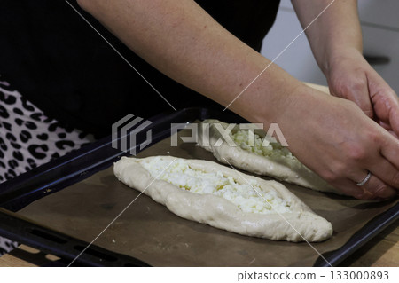 Woman folding dough into a boat shape, shredded suluguni cheese on the dough, preparing a Georgian cuisine dish, khachapuri.  133000893