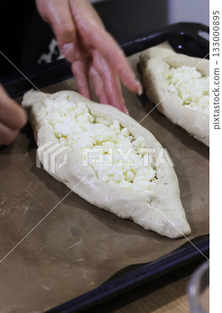 Woman folding dough into a boat shape, shredded suluguni cheese on the dough, preparing a Georgian cuisine dish, khachapuri. Close-up Woman folding dough into a boat shape, shredded suluguni cheese on the dough, preparing a Georgian cuisine dish, khachapuri. Close-up 133000895