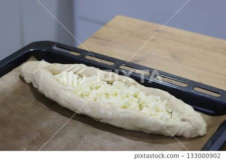 Dough shaped like a boat on a baking tray before baking, topped with shredded suluguni cheese, preparing a Georgian cuisine dish, khachapuri 133000902