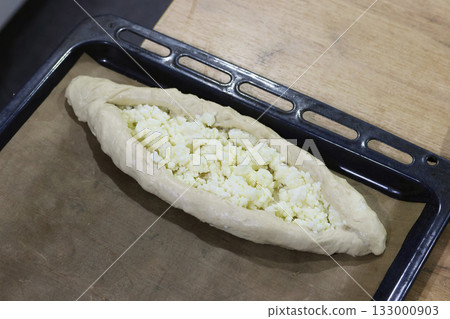 Dough shaped like a boat on a baking tray before baking, topped with shredded suluguni cheese, preparing a Georgian cuisine dish, khachapuri Dough shaped like a boat on a baking tray before baking, topped with shredded suluguni cheese, preparing a Georgian cuisine dish, khachapuri 133000903