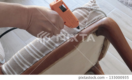 Anonymous person applies glue with glue gun and attaches tape. Antique furniture restoration. Crafts and hobbies. 133000935