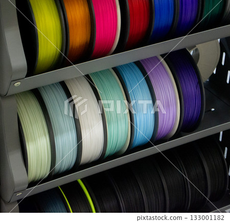 Many spools with multi-colored plastic for 3D printing. Spools with blue, green, white, purple plastic wire for 3D printer. Components for 3D printing. Accessories for 3D printer. FDM technology Many spools with multi-colored plastic for 3D printing. Spools with blue, green, white, purple plastic wire for 3D printer. Components for 3D printing. Accessories for 3D printer. FDM technology 133001182