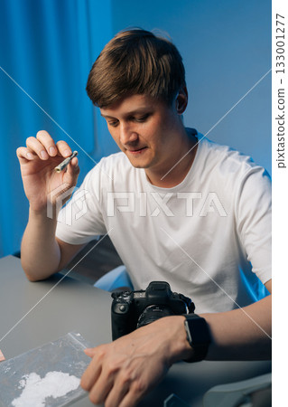 Vertical shot of photographer preparing illegal substance using rolled currency, sitting at table with camera, revealing personal struggle with drug dependency. Concept of addiction, substance abuse. 133001277