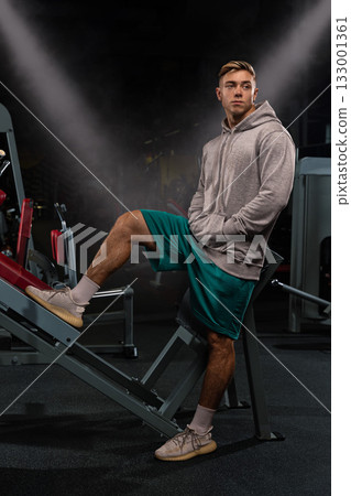 athletic individual in a gray hoodie poses confidently in a gym showcasing strength and determination. athletic individual in a gray hoodie poses confidently in a gym showcasing strength and determination. 133001361