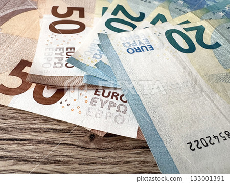 A close-up of euro banknotes fanned out on a wooden table. Fragments of 50- and 20-euro notes. A close-up of euro banknotes fanned out on a wooden table. Fragments of 50- and 20-euro notes. 133001391