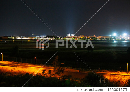 Night view of an airport with illuminated runways and distant city lights Night view of an airport with illuminated runways and distant city lights 133001575