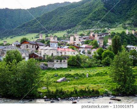 houses in Mestia town on green slope near river 133001975