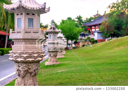 Stone lanterns line a path in Nanshan Park, surrounded by greenery. Chinese architecture is visible in the background. Stone lanterns line a path in Nanshan Park, surrounded by greenery. Chinese architecture is visible in the background. 133002288