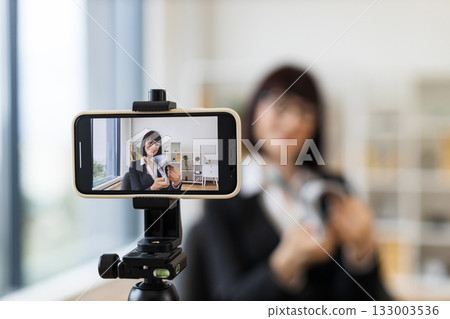 Professional setting with Caucasian adult woman presenting financial concepts through video blogging setup with cash. 133003536