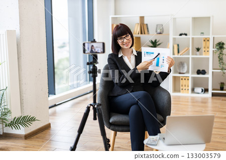 Caucasian woman, business professional, presenting growth graphs during vlog in modern office setup. 133003579