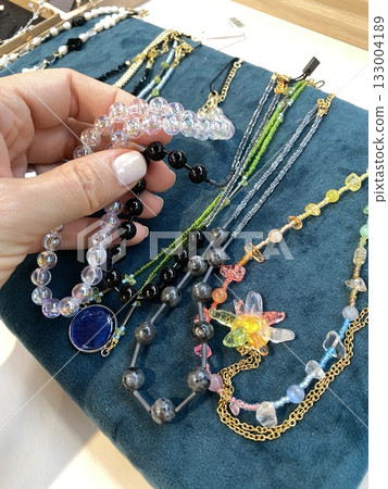Hand holding colorful beaded necklaces on display against teal fabric background 133004189