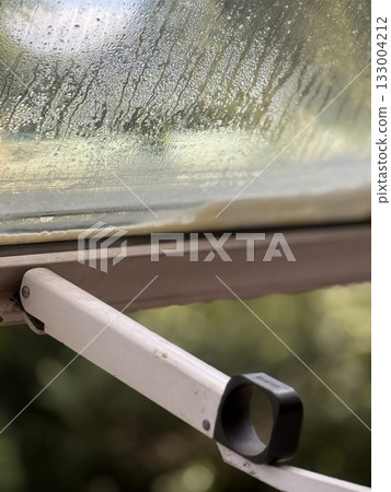 Rainy day seen through open window with raindrops on glass, creating natural background Rainy day seen through open window with raindrops on glass, creating natural background 133004212